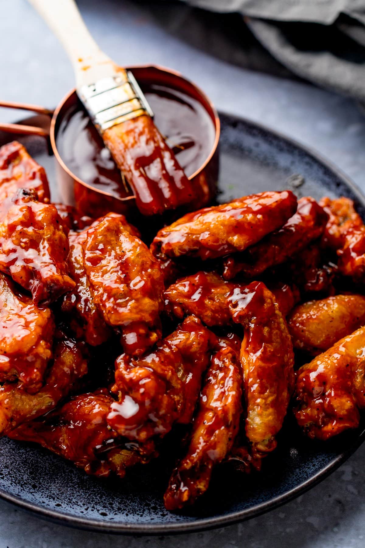 BBQ chicken wings on a black plate with a pot of BBQ sauce and a brush on top.