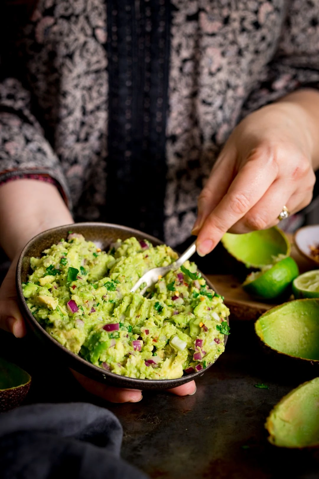 Close up of hands stirring together guacamole in a bowl..