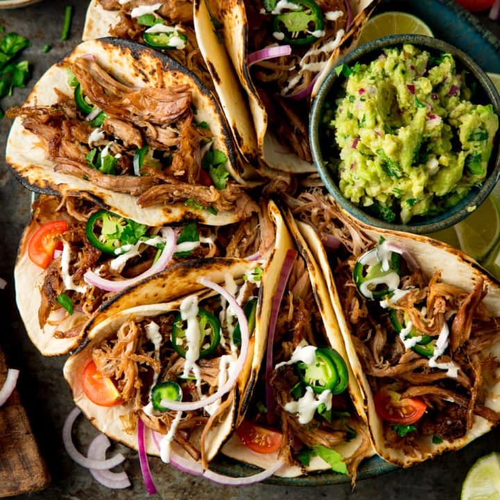 Square image of a plate of Lamb Barbacoa Carnita Tacos with a bowl of guacamole