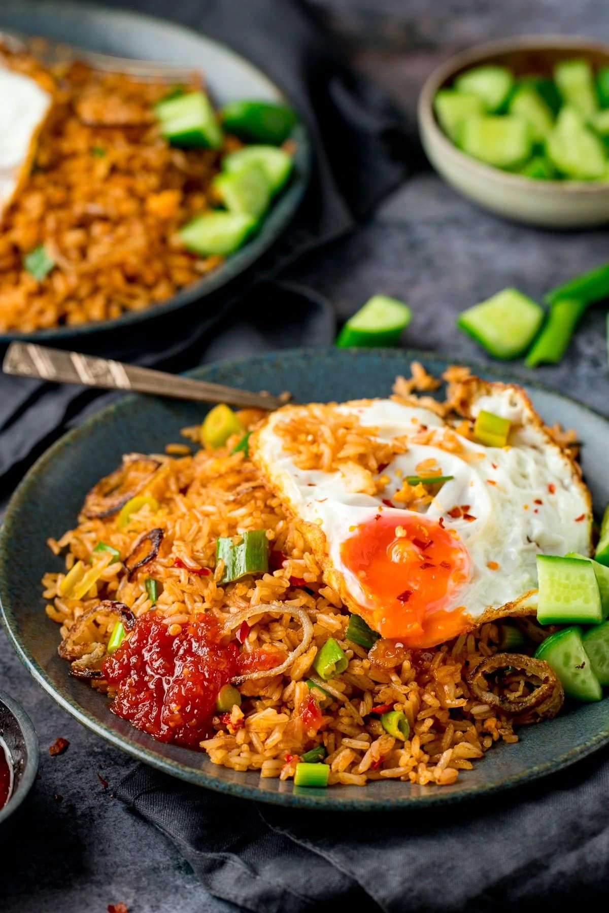 nasi goreng rice on a plate, with a fried egg, chilli sauce and cucumber