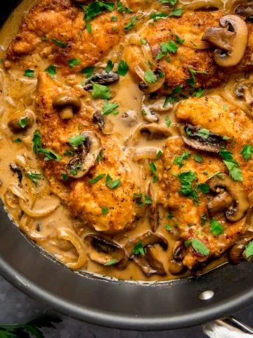 chicken marsala in a pan with mushroom and onions, sprinkled with fresh parsley