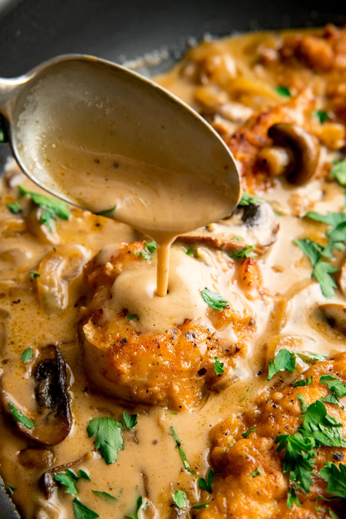 Creamy sauce being spooned over chicken marsala in a pan