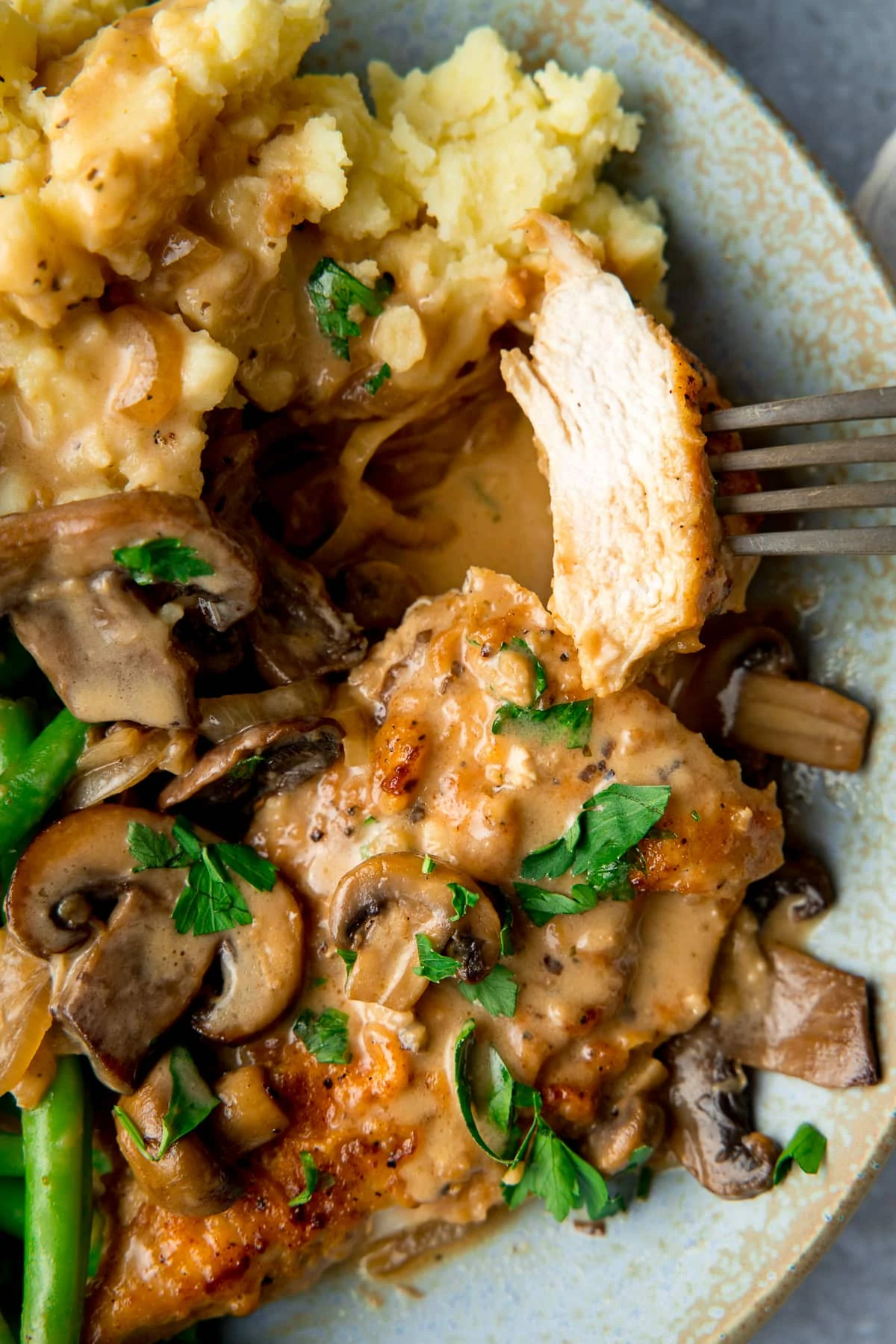 chicken marsala on a plate with mashed potato and green beans. Forkful of chicken being taken.