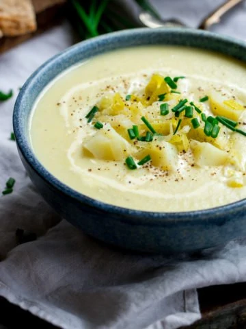 leek and potato soup in a blue bowl, topped with potatoes and chives