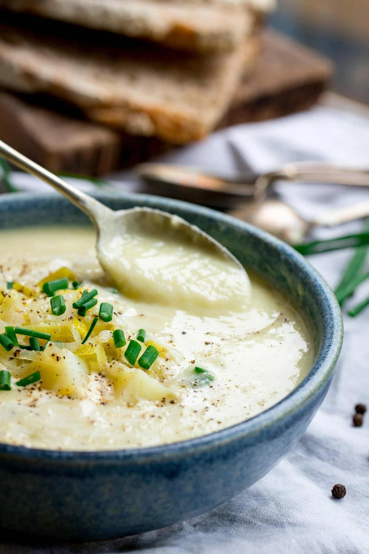 spoonful being taken from a bowl of leek and potato soup. Bowl is blue. Sliced bread in the background.