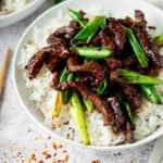 Mongolian Beef and spring onions on top of rice in a white bowl