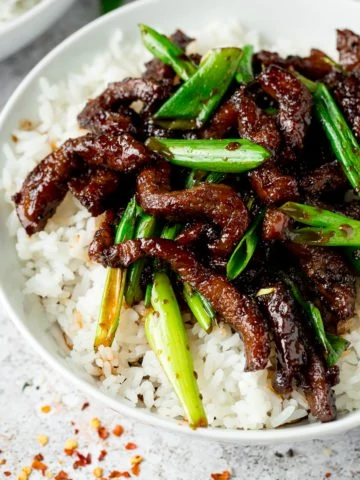 Mongolian Beef and spring onions on top of rice in a white bowl