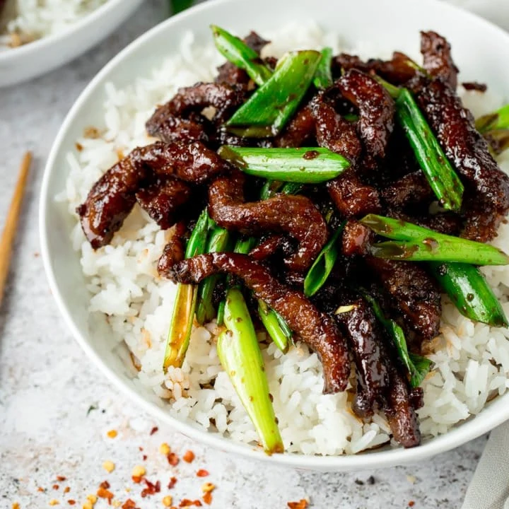 Mongolian Beef and spring onions on top of rice in a white bowl