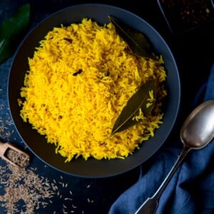 Square image of Pilau rice in a black bowl on a dark surface