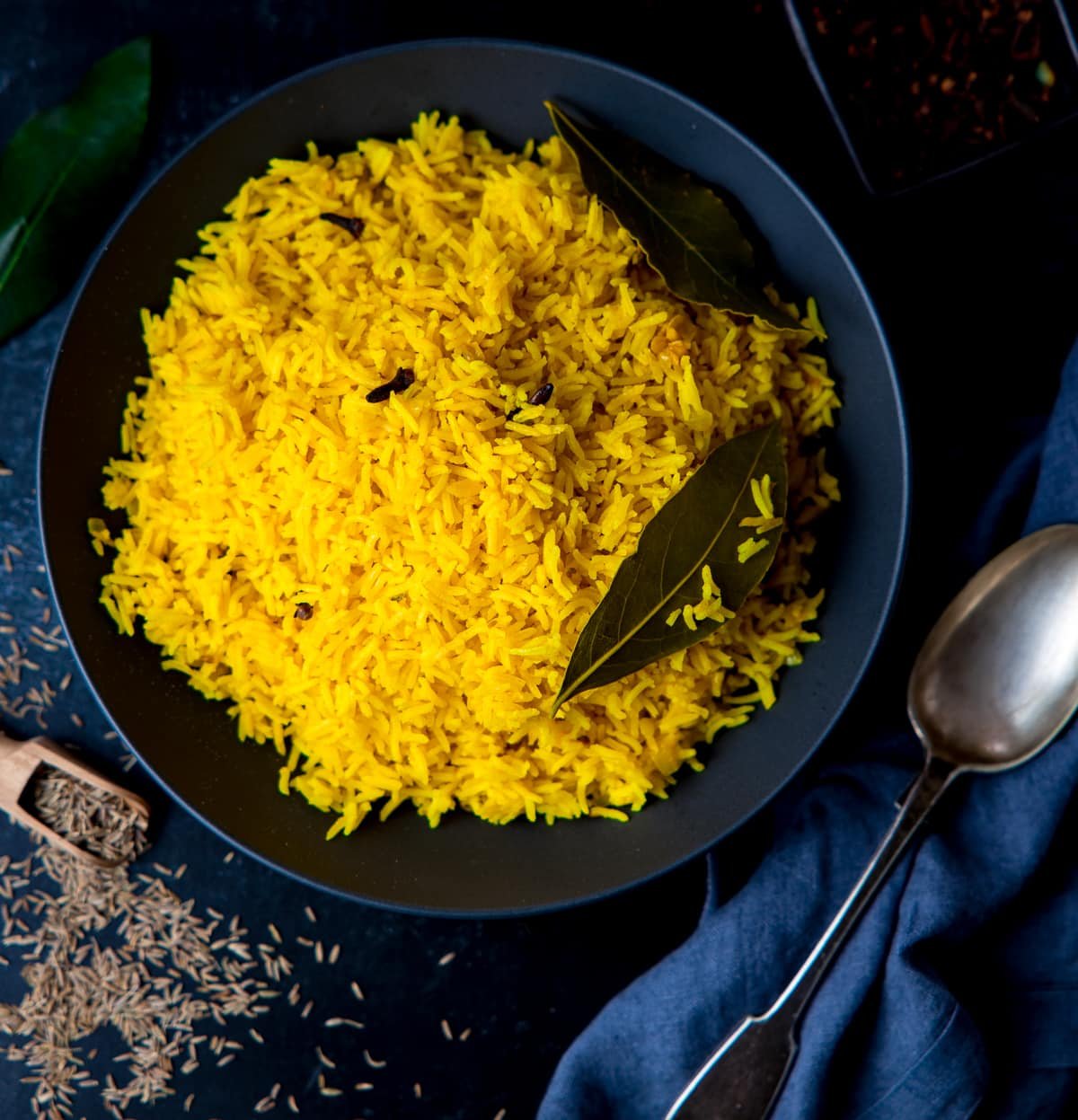 Square image of Pilau rice in a black bowl on a dark surface