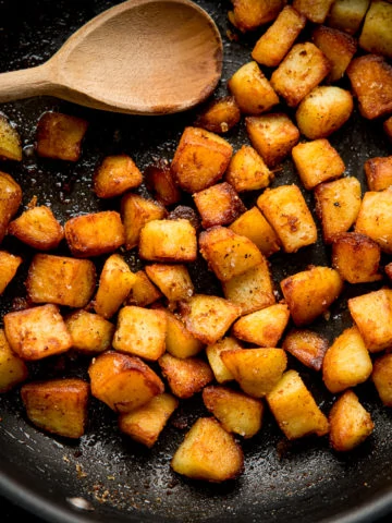 Square image of saute potatoes in a pan with a wooden spoon