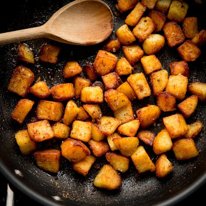 Square image of saute potatoes in a pan with a wooden spoon