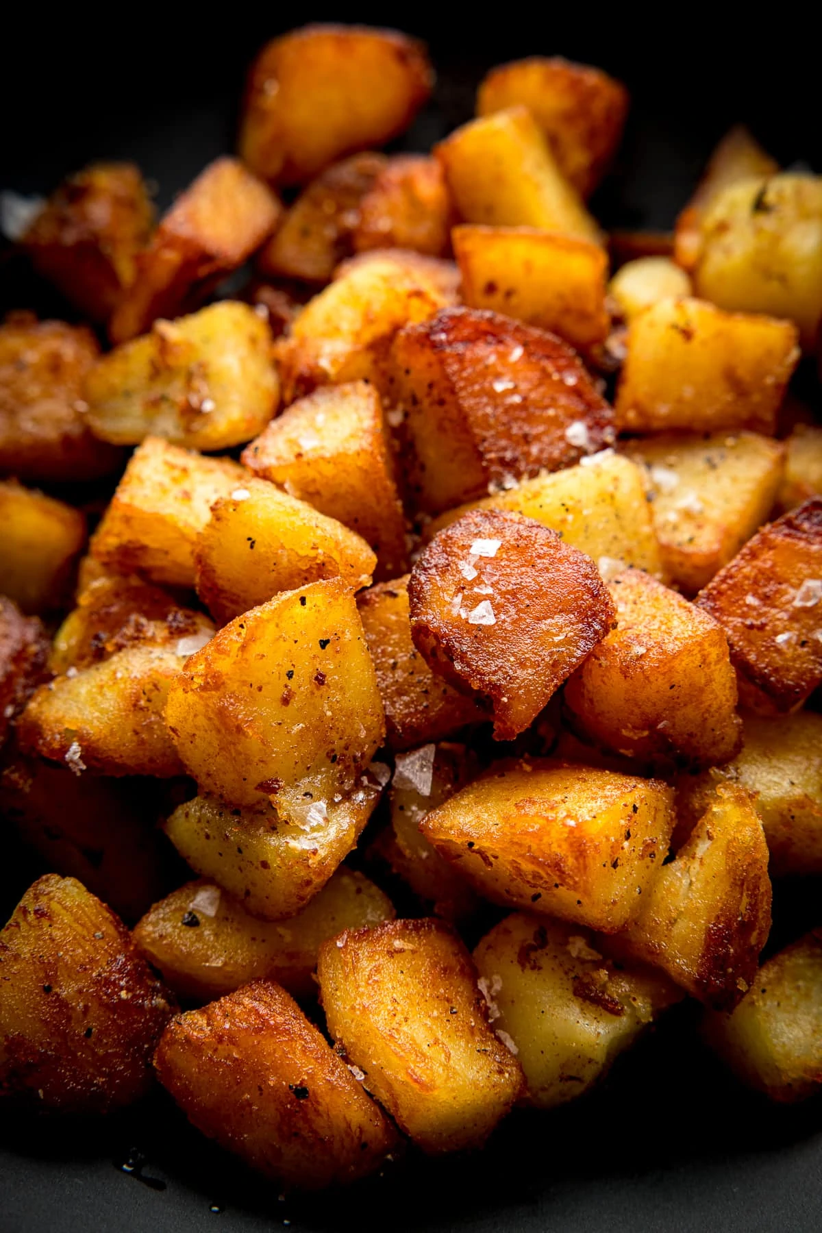 Close up image of a pile of crispy saute potatoes in a dark bowl topped with a sprinkling of salt