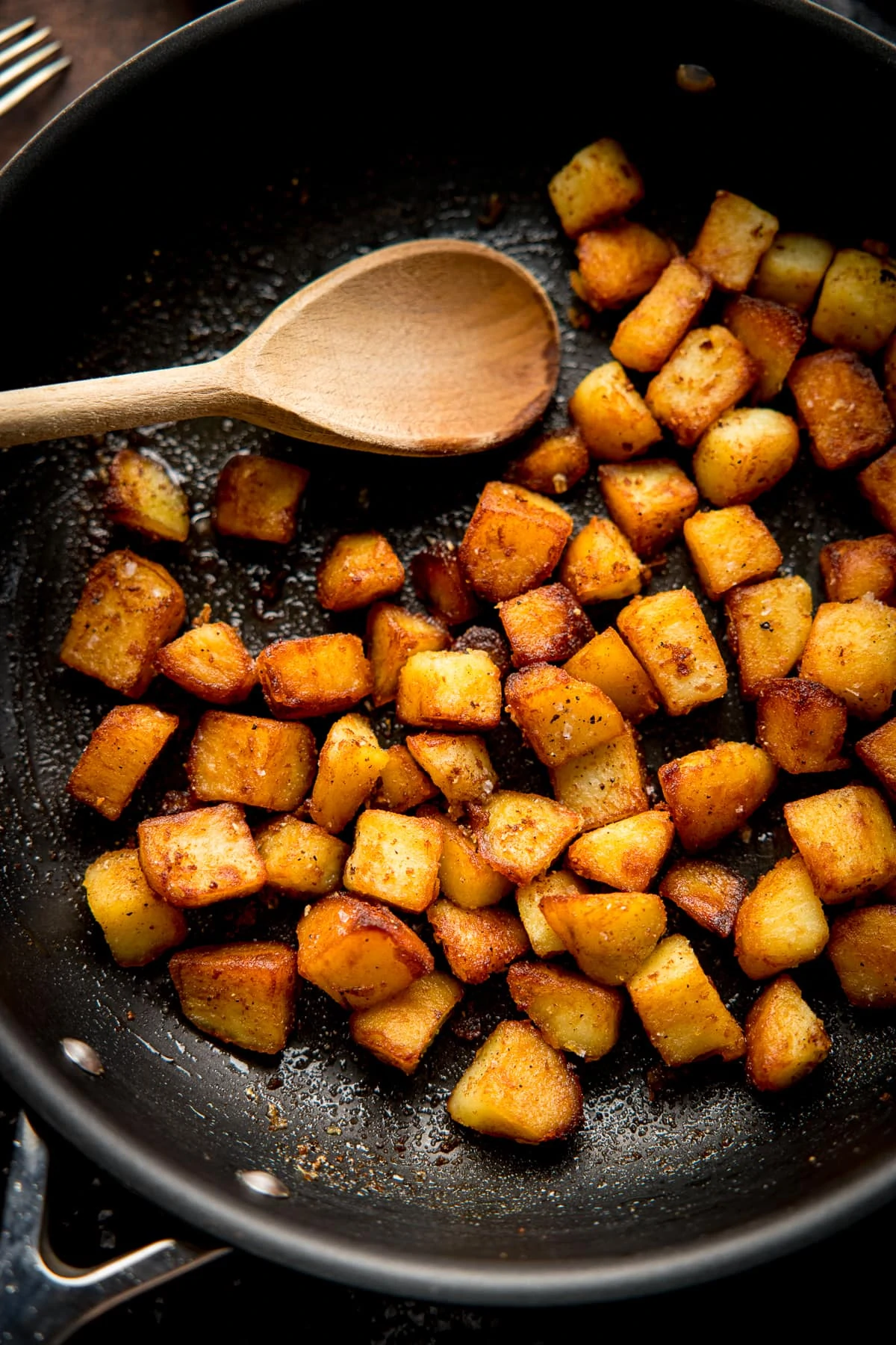 saute potatoes in a dark pan with a wooden spoon