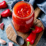 Overhead shot of sweet chilli sauce in a jar with chillies and garlic scattered around