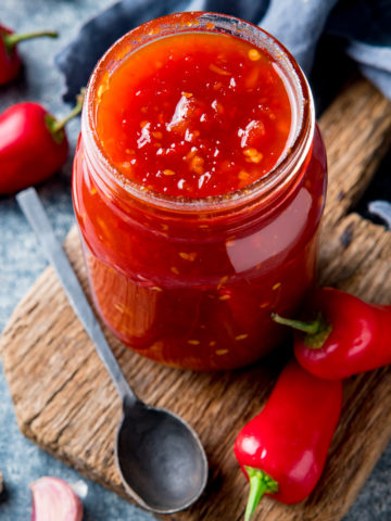 Overhead shot of sweet chilli sauce in a jar with chillies and garlic scattered around