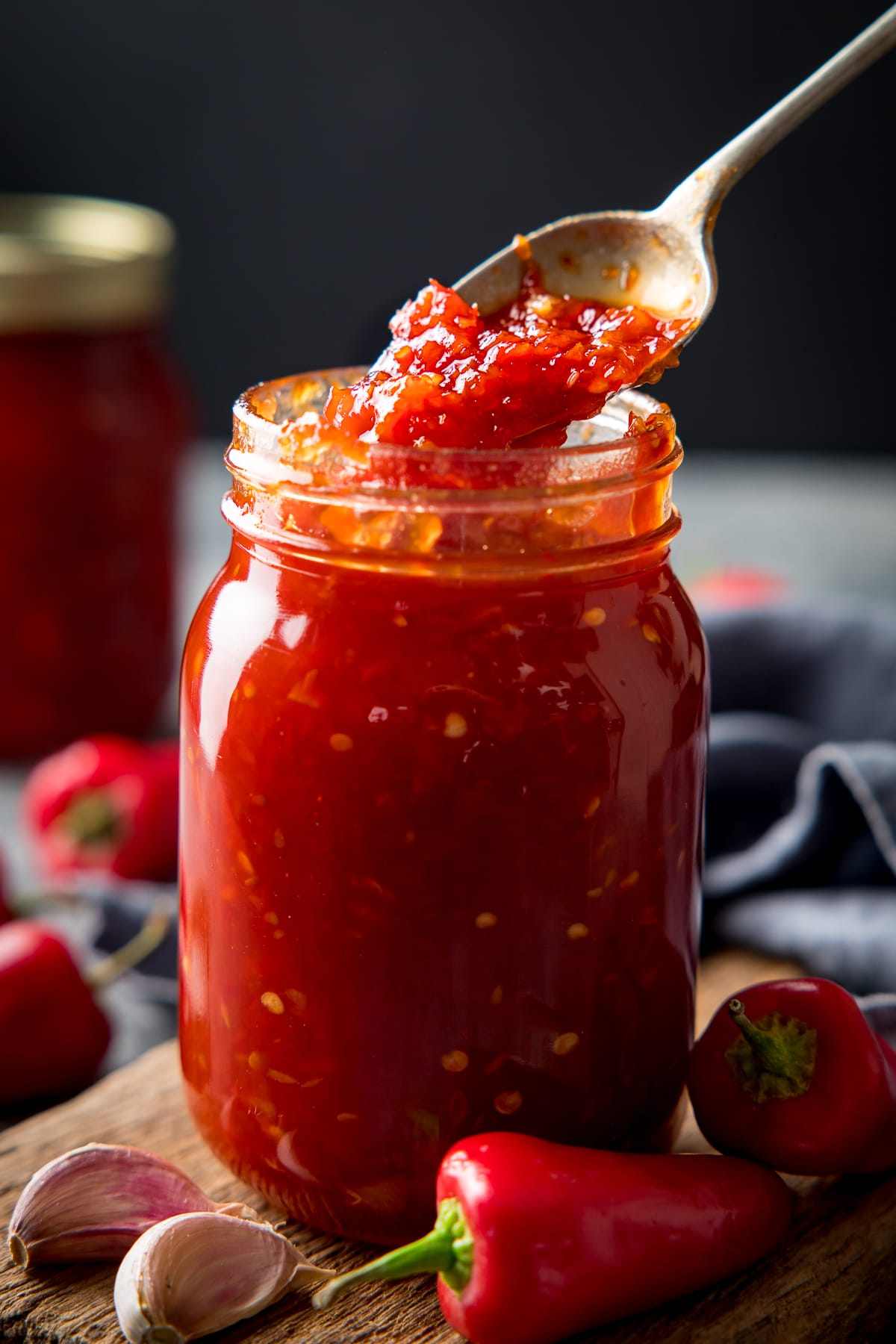 Spoonful being taken from a jar of sweet chilli sauce. Ingredients scattered around the jar.