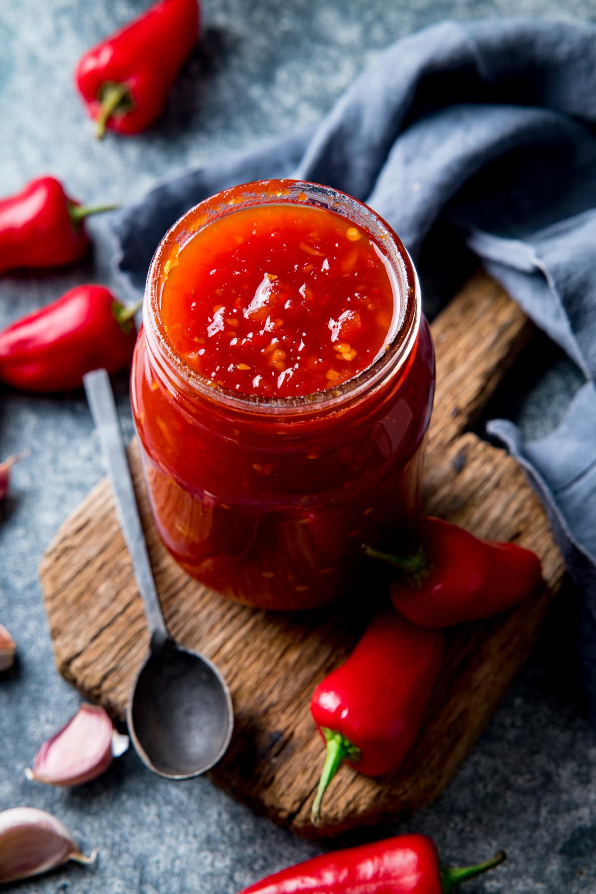Sweet chilli sauce in a jar surrounding by ingredients on a blue background