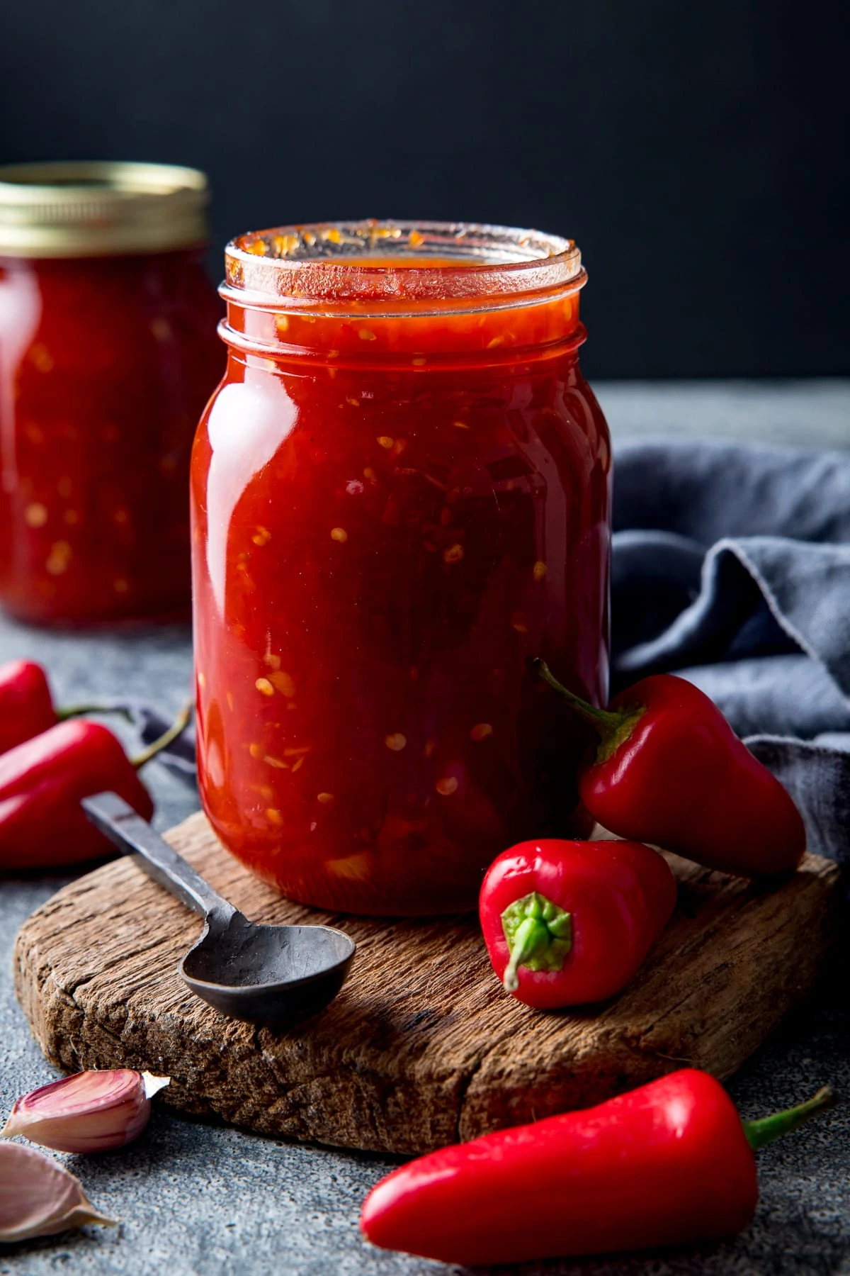 Jar of sweet chilli sauce with a board next to a spoon and some fresh chillies