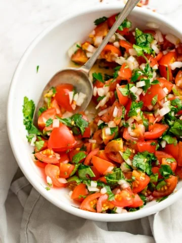 tomato, onion and coriander chopped salad in a white bowl on a light background. Spoon in the salad.