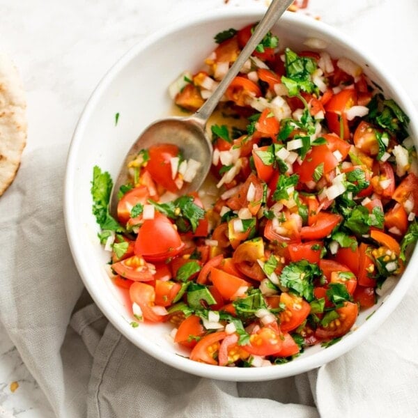 tomato, onion and coriander chopped salad in a white bowl on a light background. Spoon in the salad.