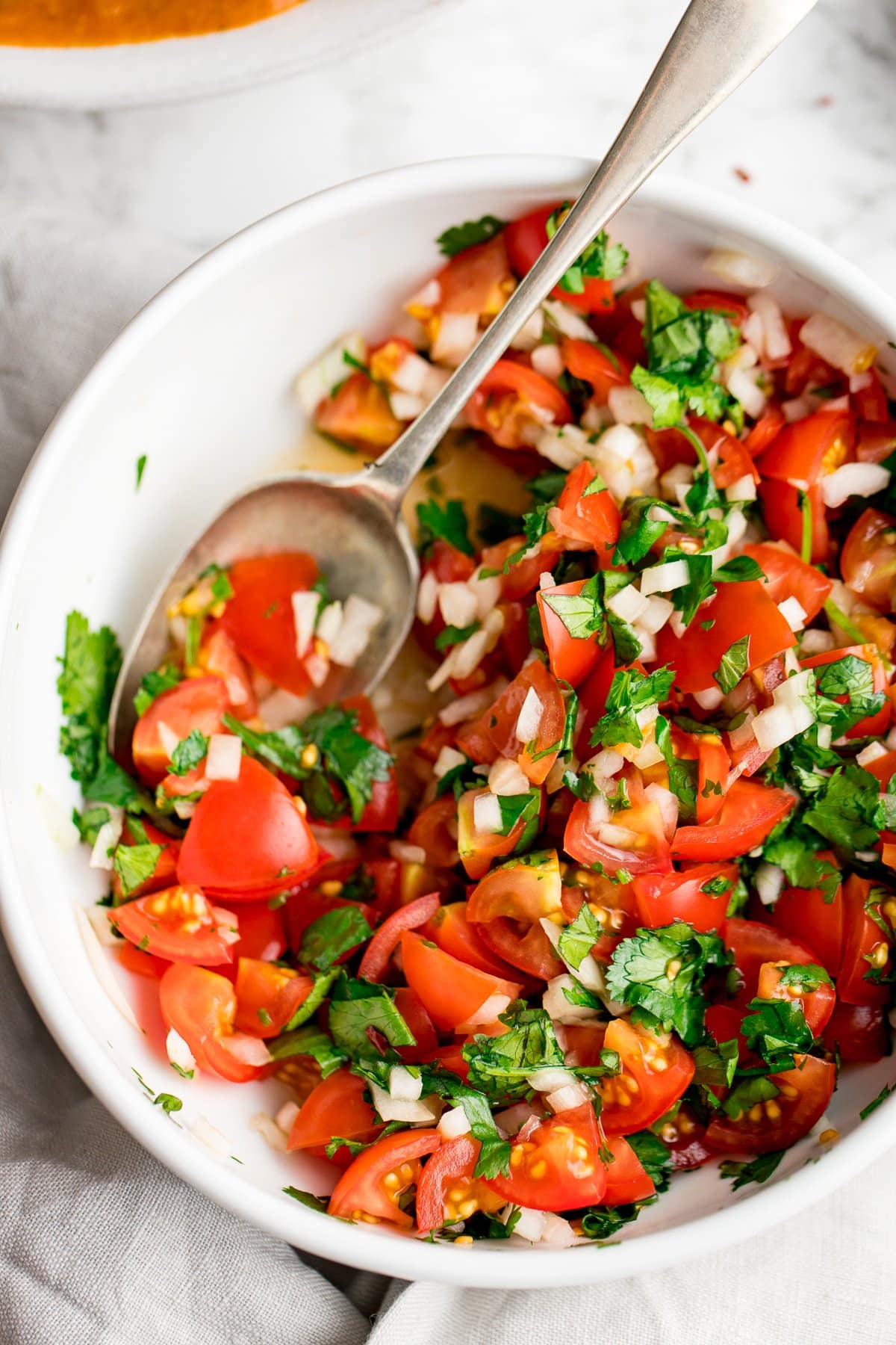tomato, onion and coriander chopped salad in a white bowl with a spoon.
