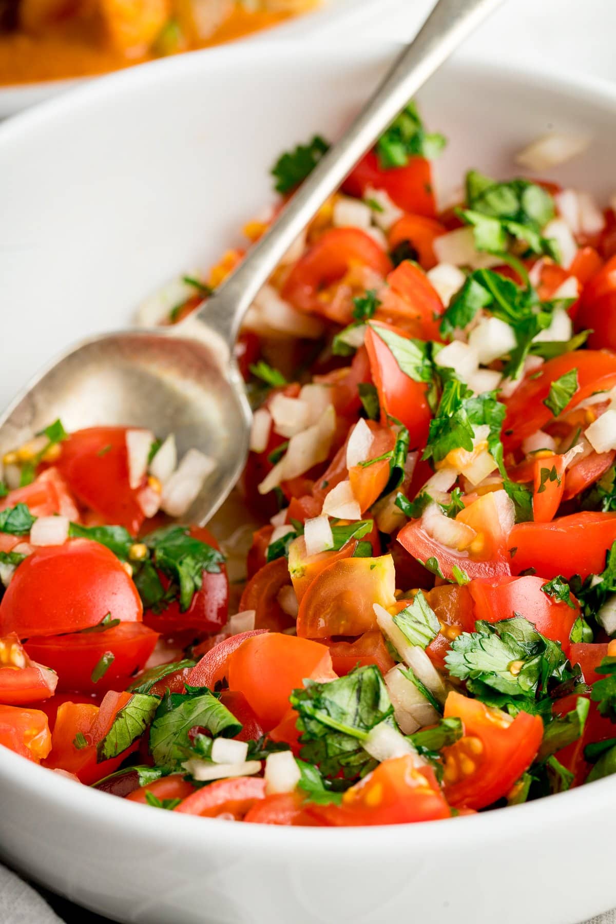 Close up of tomato, onion and coriander chopped salad in a white bowl with a spoon