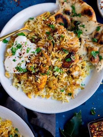 chicken biryani topped with natural yogurt on a white plate on a blue background.