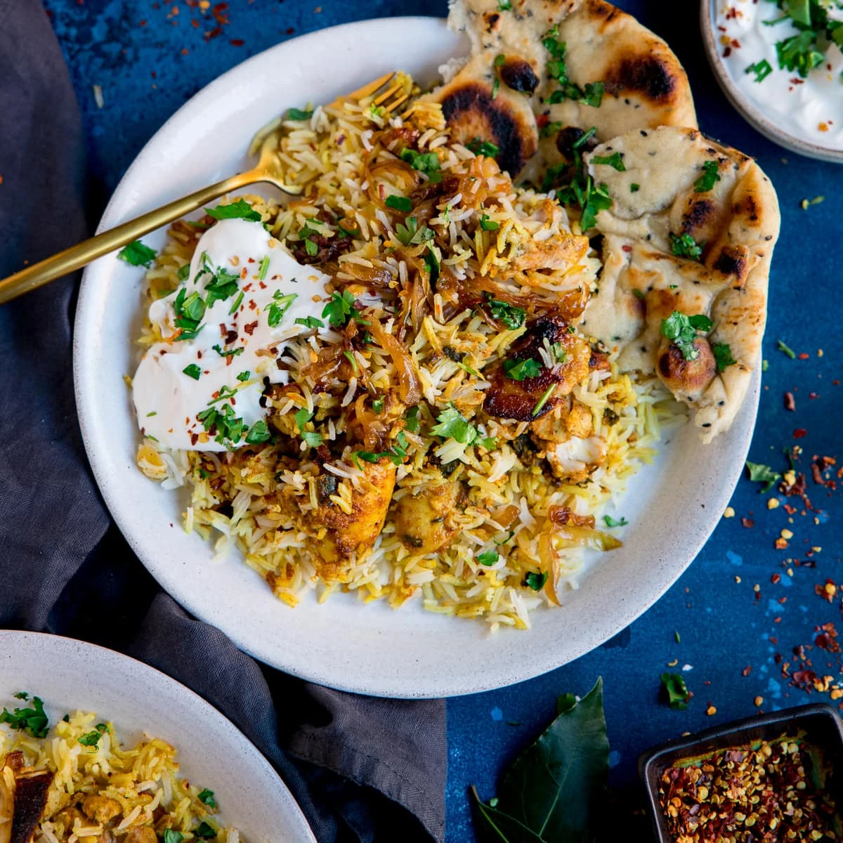 chicken biryani topped with natural yogurt on a white plate on a blue background.