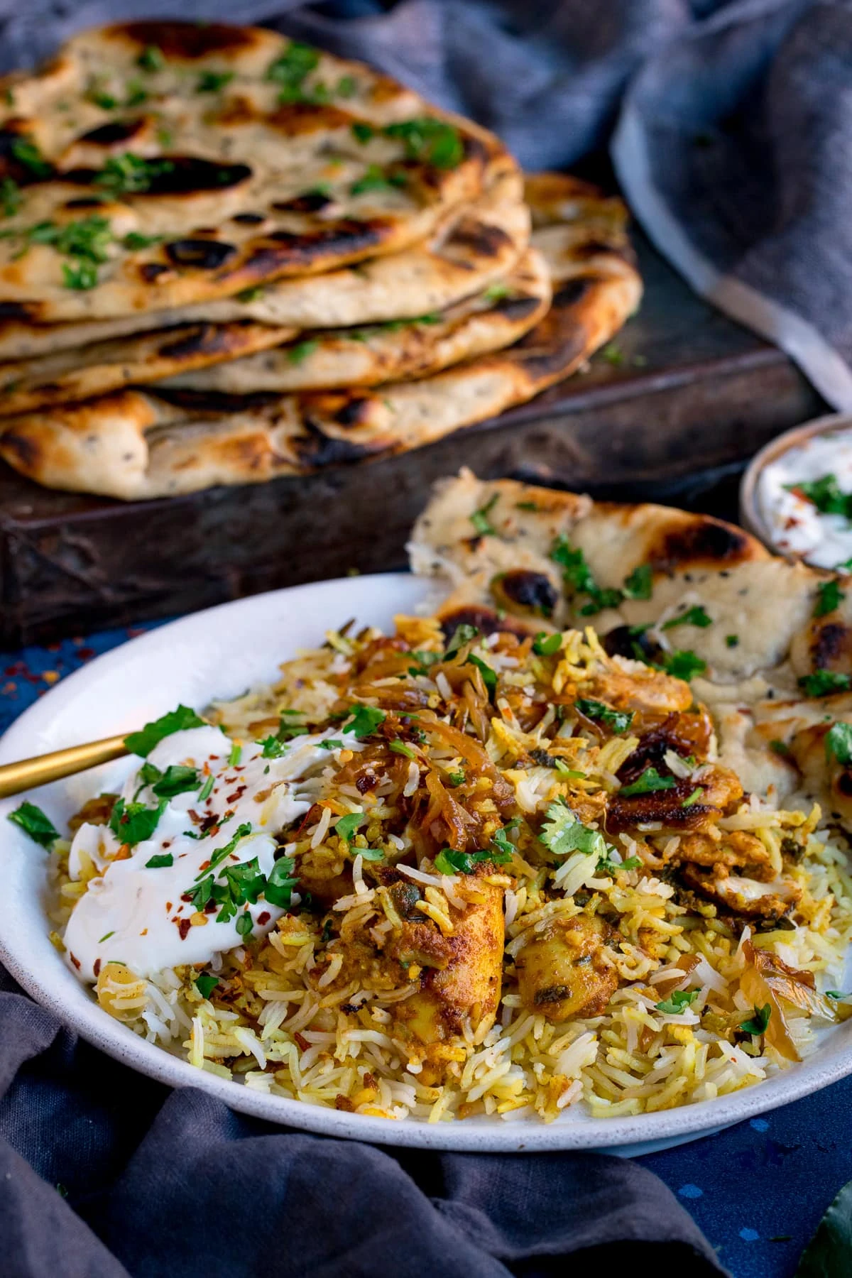 Plate of chicken biryani with pile of naan breads in the background