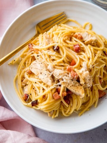 chicken carbonara in a white bowl with a gold fork
