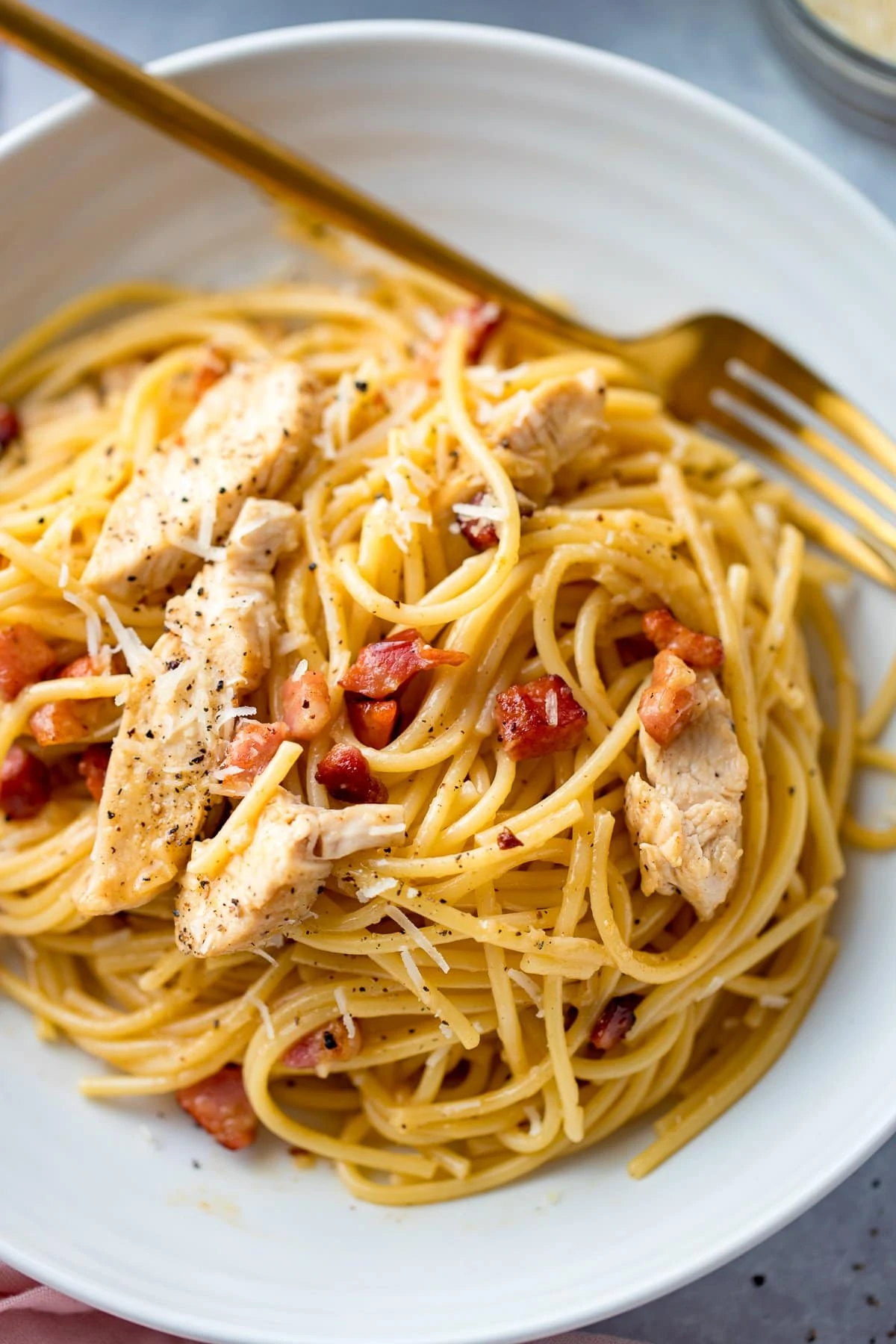 Overhead image of chicken carbonara in a white bowl with a fork