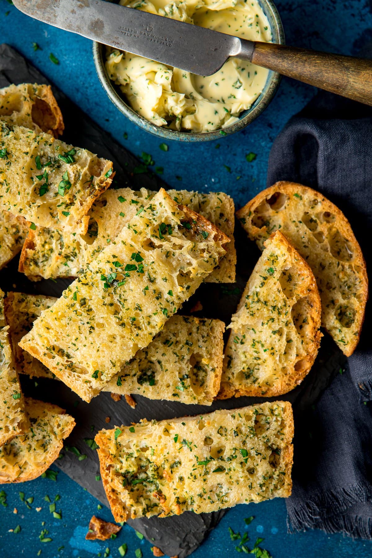 Overhead of slices of garlic bread on a dark background with bowl of garlic butter at top of the frame