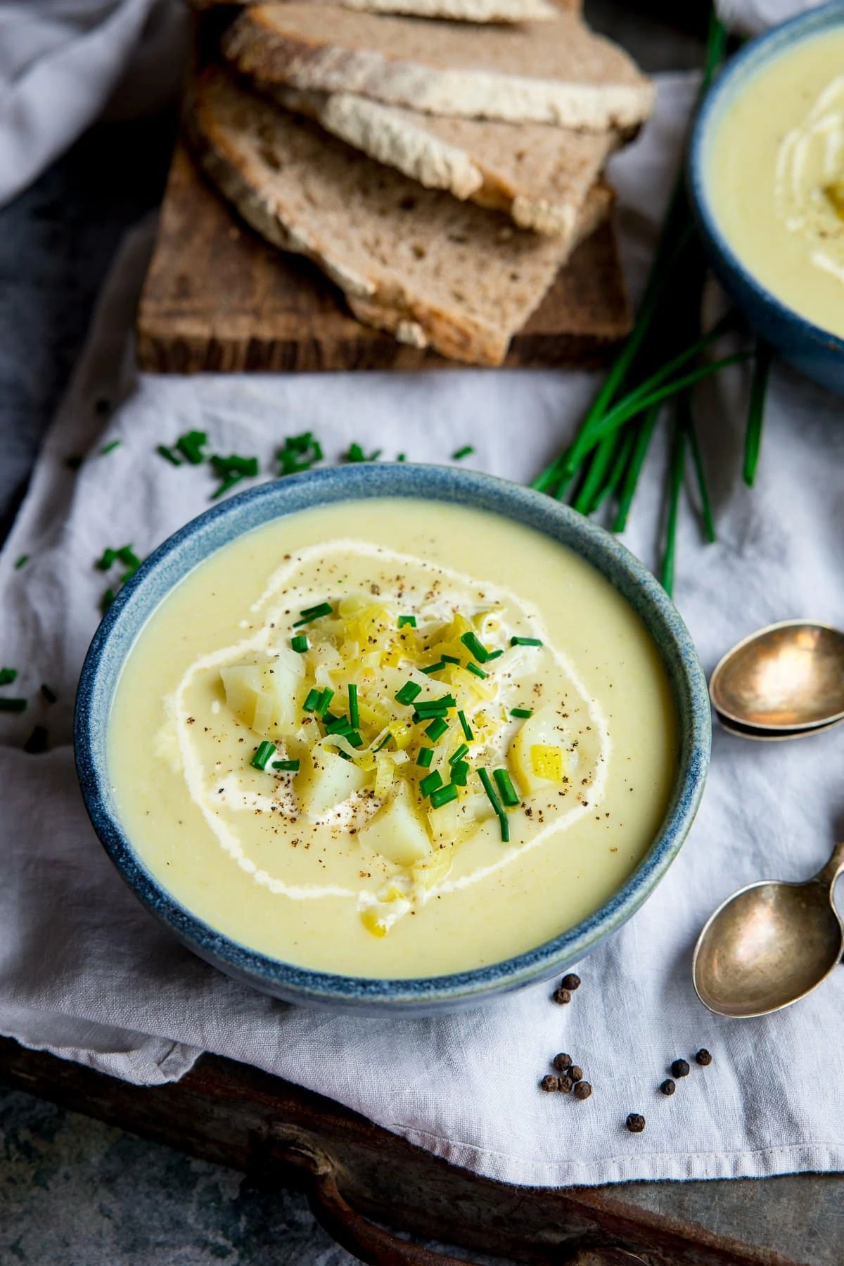 leek and potato soup in a blue bowl on top of a napkin. Sliced bread and further bowl at the top of the shot.