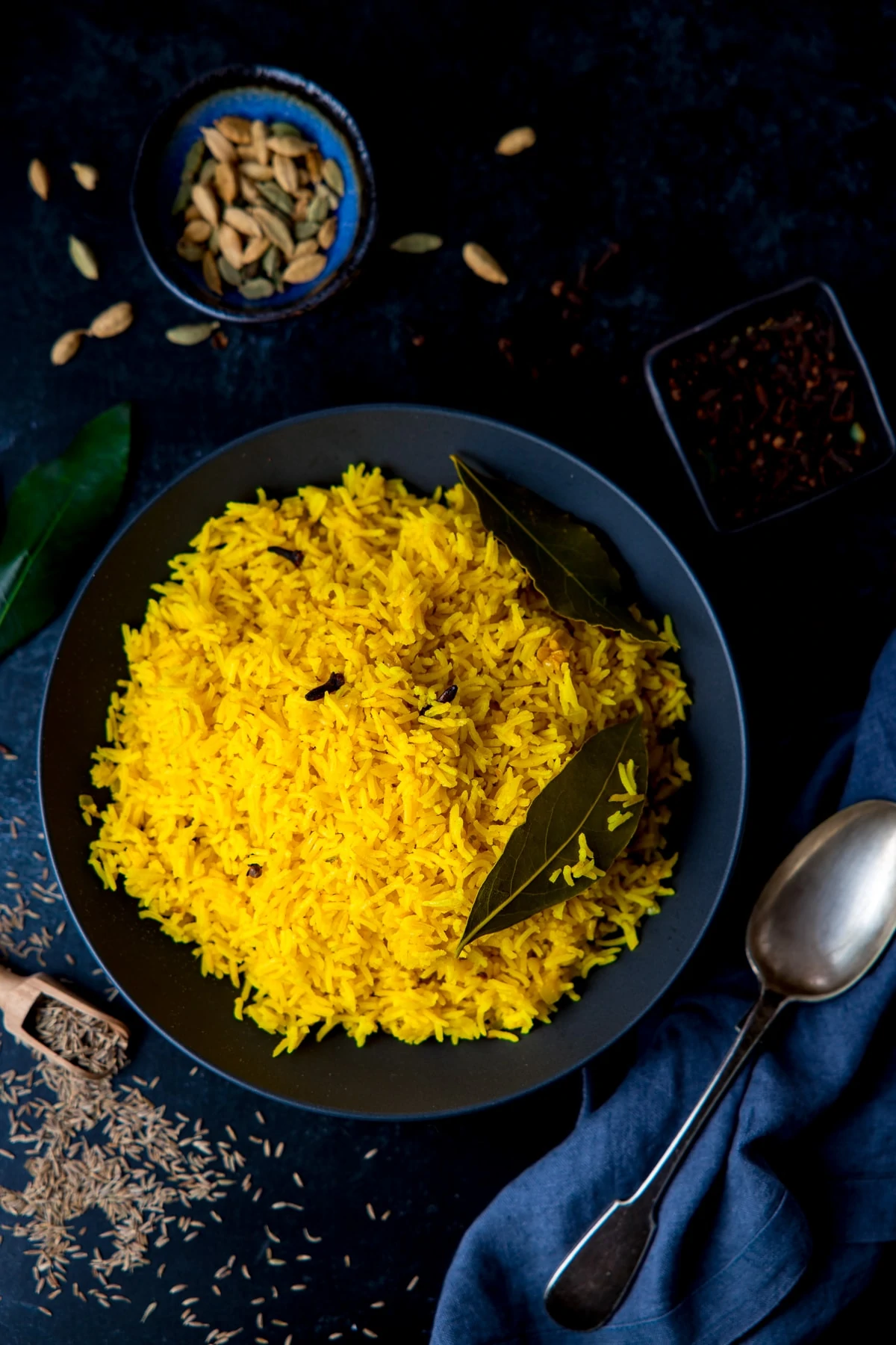 Pilau rice in a black bowl on a dark surface with ingredients scattered around