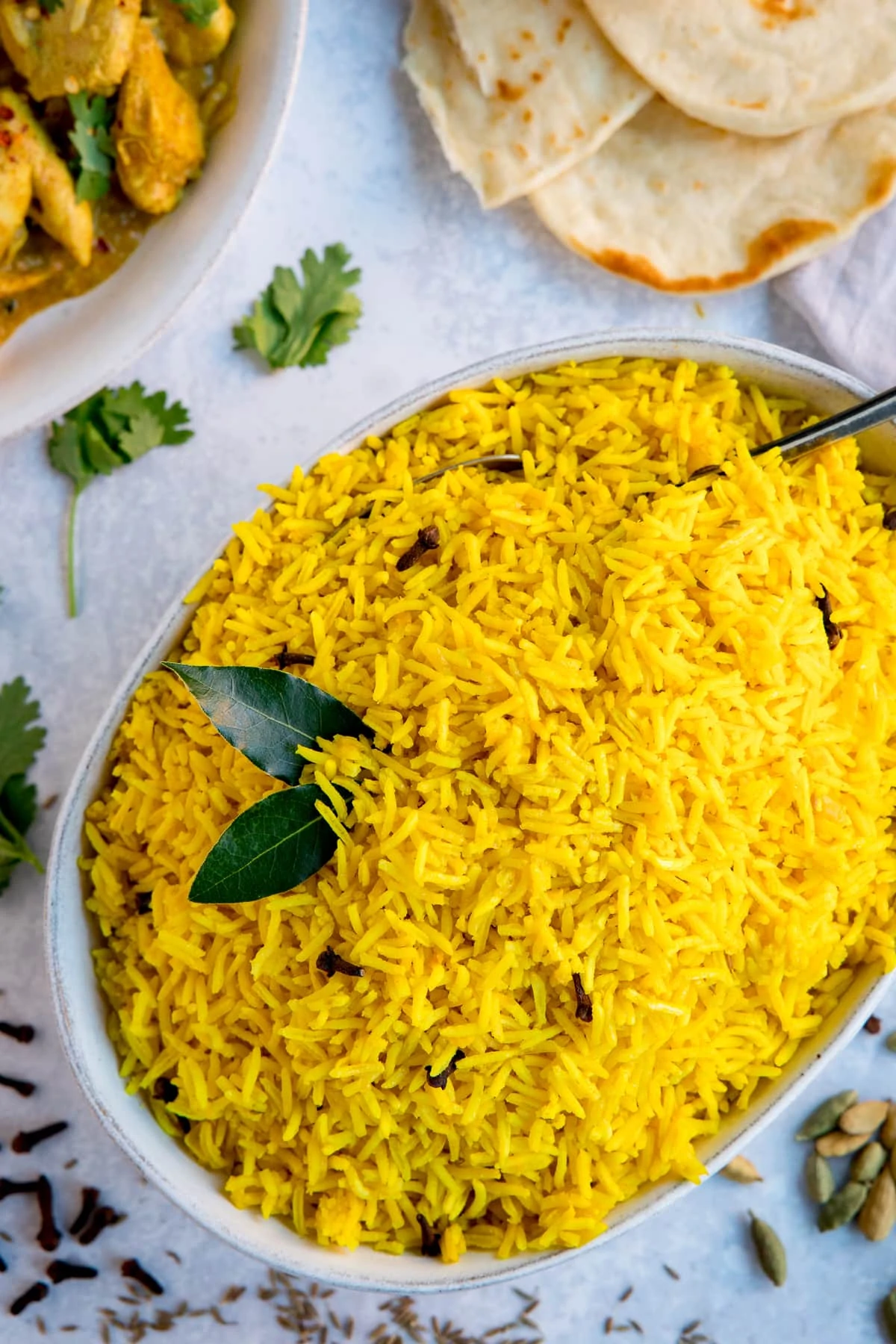Pilau rice in a white bowl on a light background. Flatbreads and plate of curry just in frame