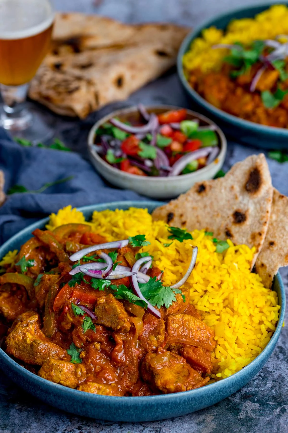 Pilau rice with chicken jalfrezi in a blue bowl on a blue background. Further dishes scattered around.