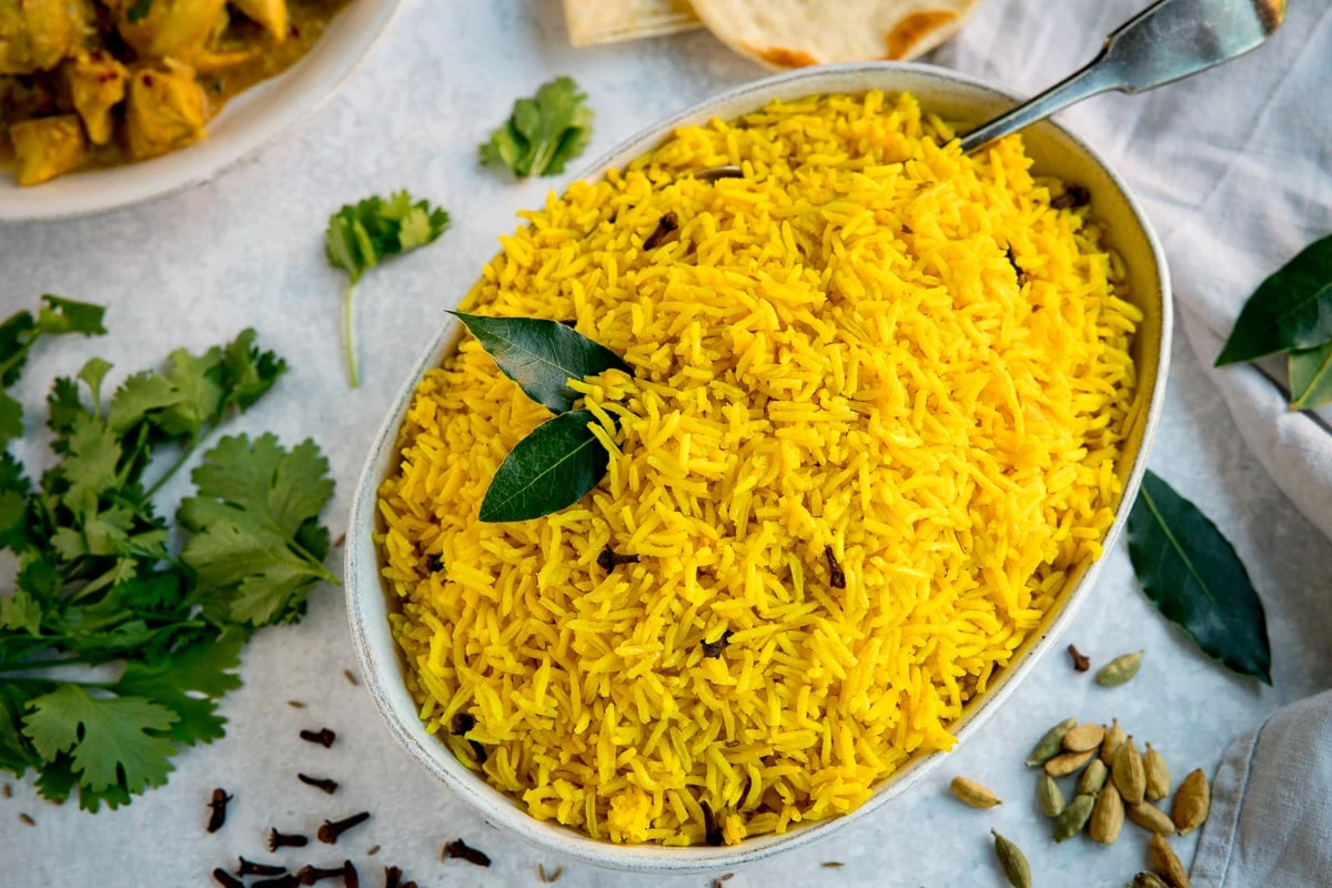 Wide image of Pilau rice in a white oblong bowl on a white surface.