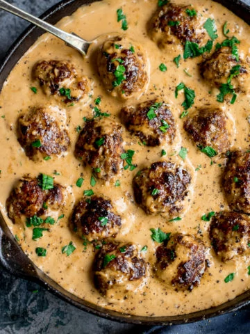 Swedish meatballs and gravy in a pan on a mottled blue background.