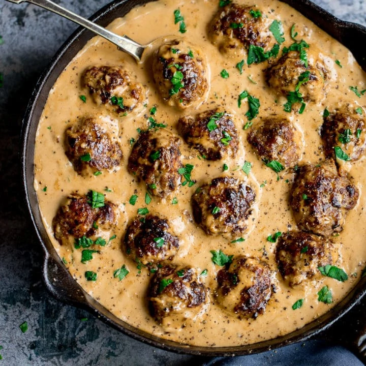 Swedish meatballs and gravy in a pan on a mottled blue background.