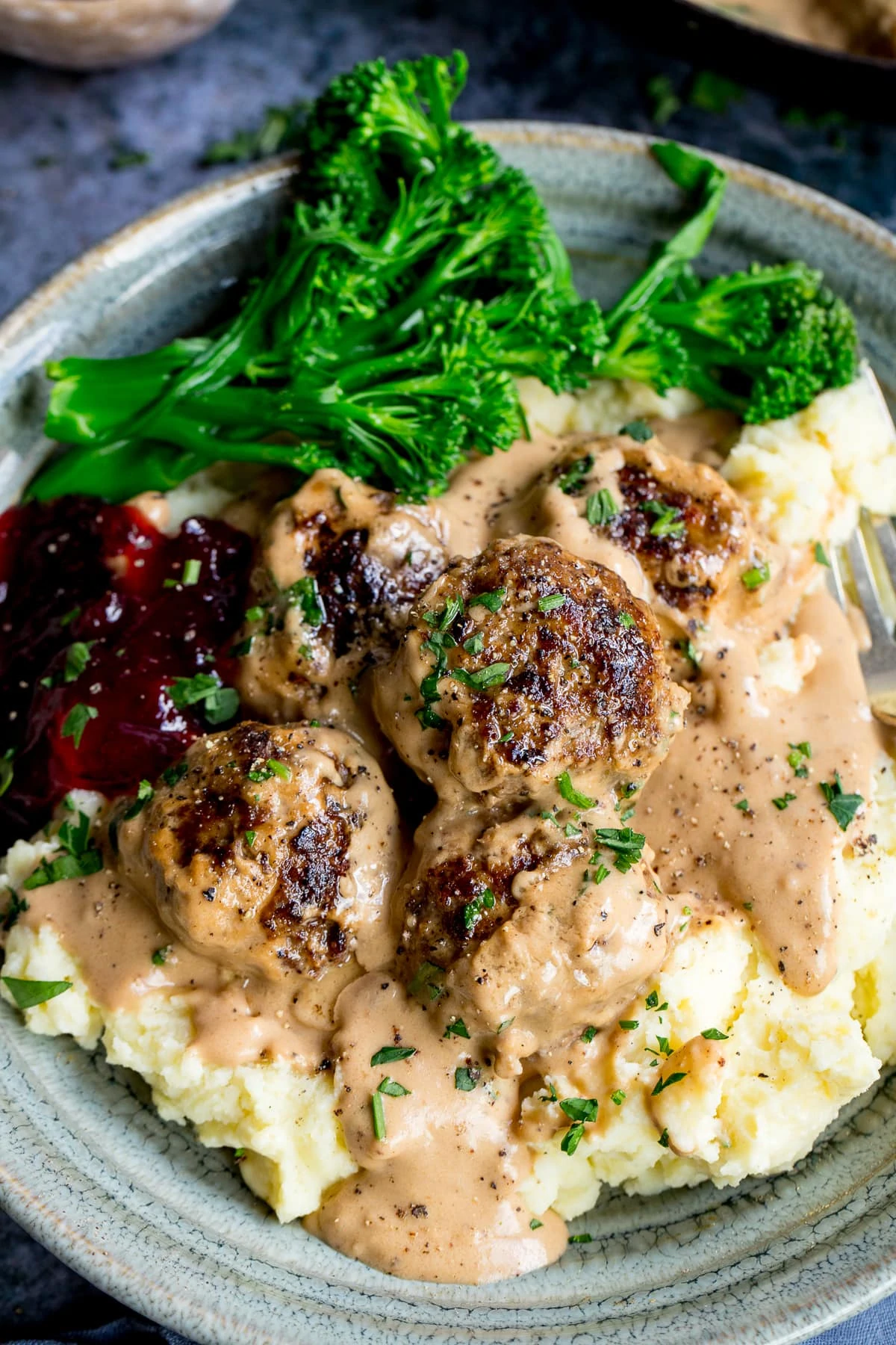 Swedish meatballs on top of mashed potatoes in a bowl with lingonberry jam and broccoli