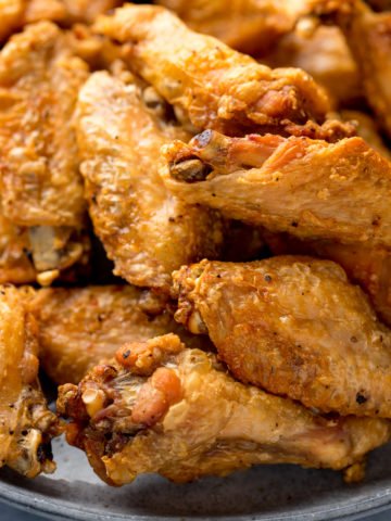 Close up image of crispy chicken wings piled up on a grey plate.