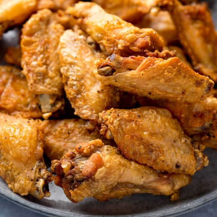 Close up image of crispy chicken wings piled up on a grey plate.