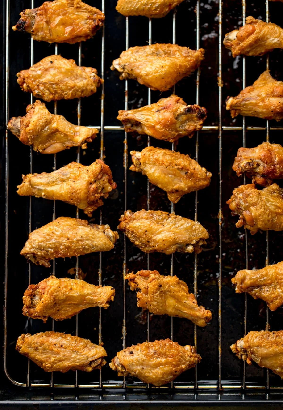 Overhead shot of crispy chicken wings lined up on a wire rack over a dark tray.