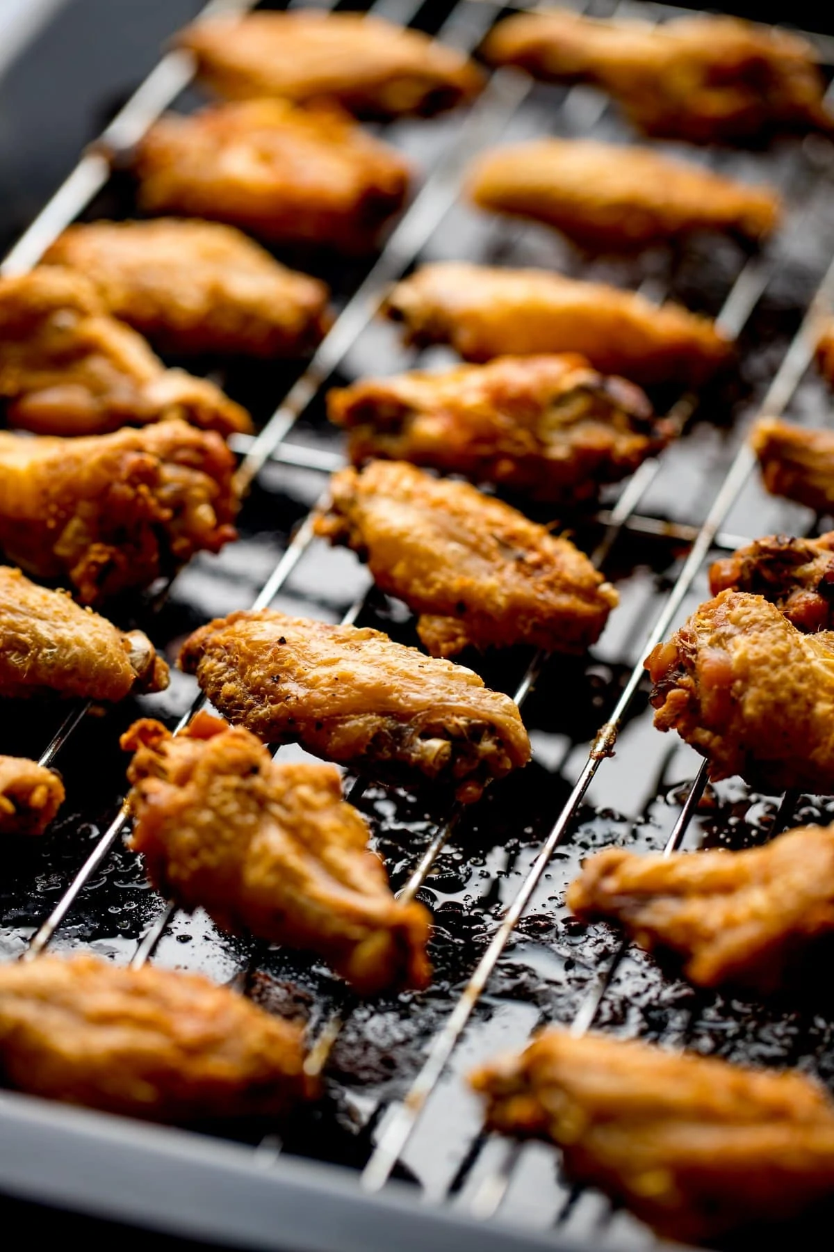 Cooked crispy chicken wings on a wire rack over a dark tray.