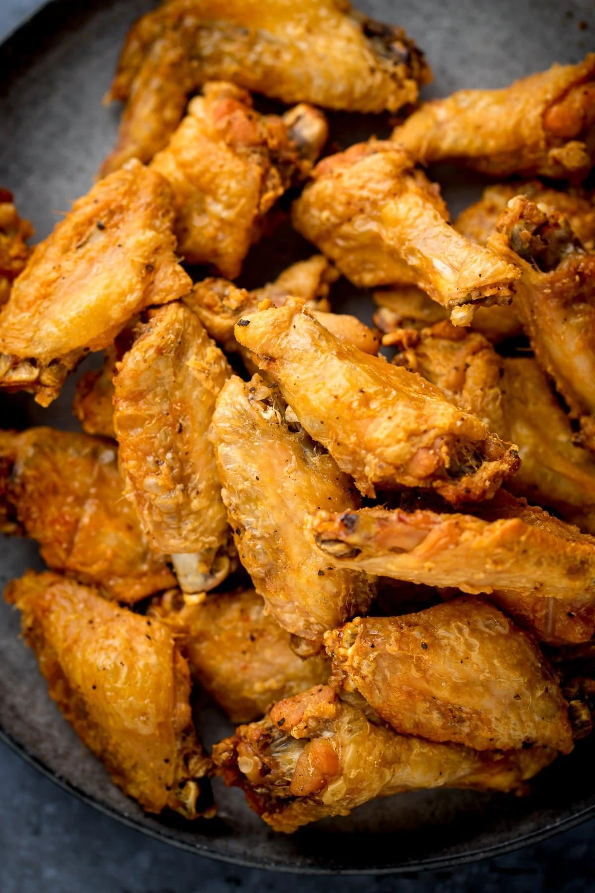 Pile of crispy chicken wings on a dark plate.
