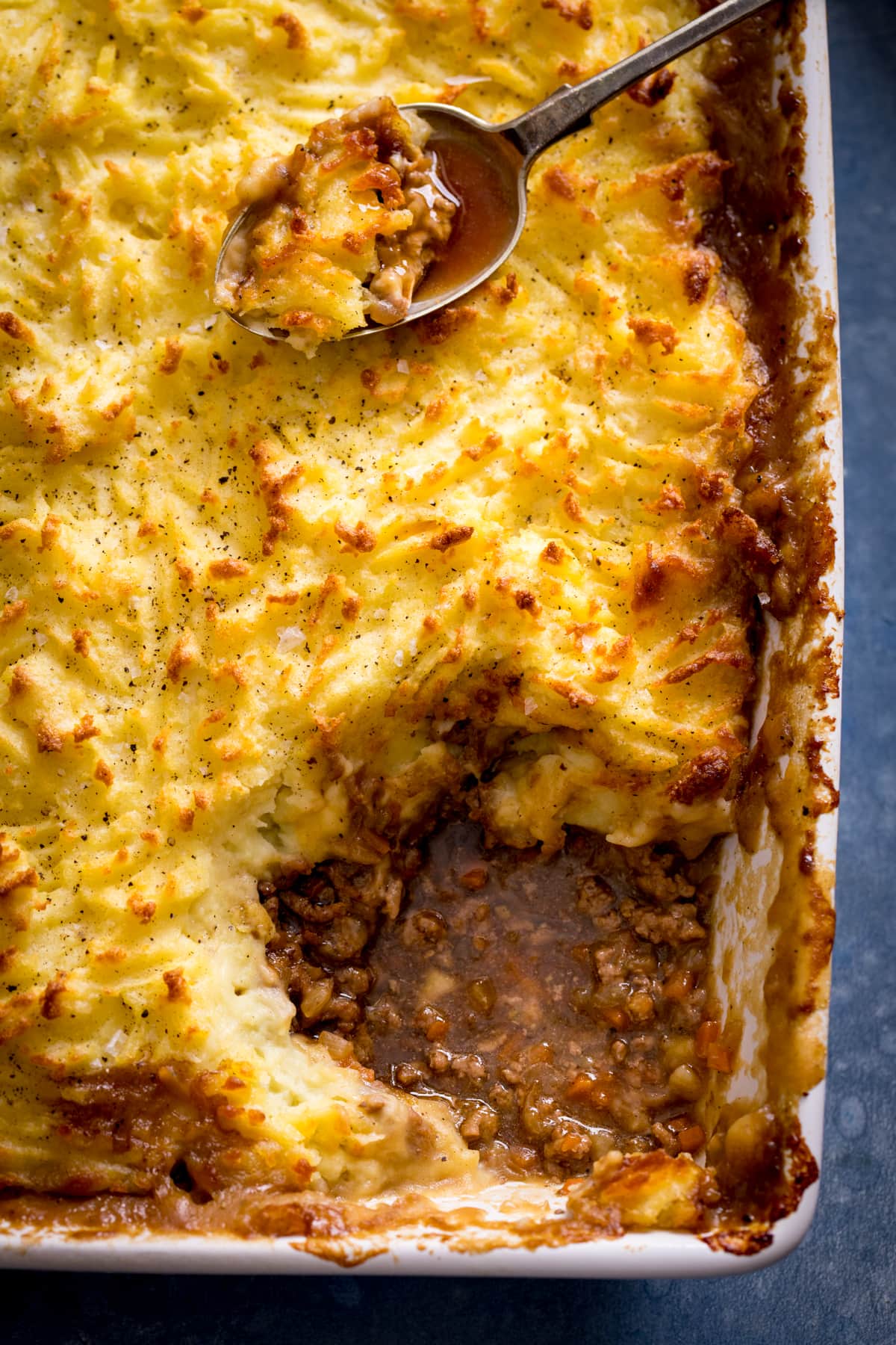 Close of of Shepherd's pie with a portion taken out and a spoon with Shepherd's pie resting on top of the Shepherd's pie.