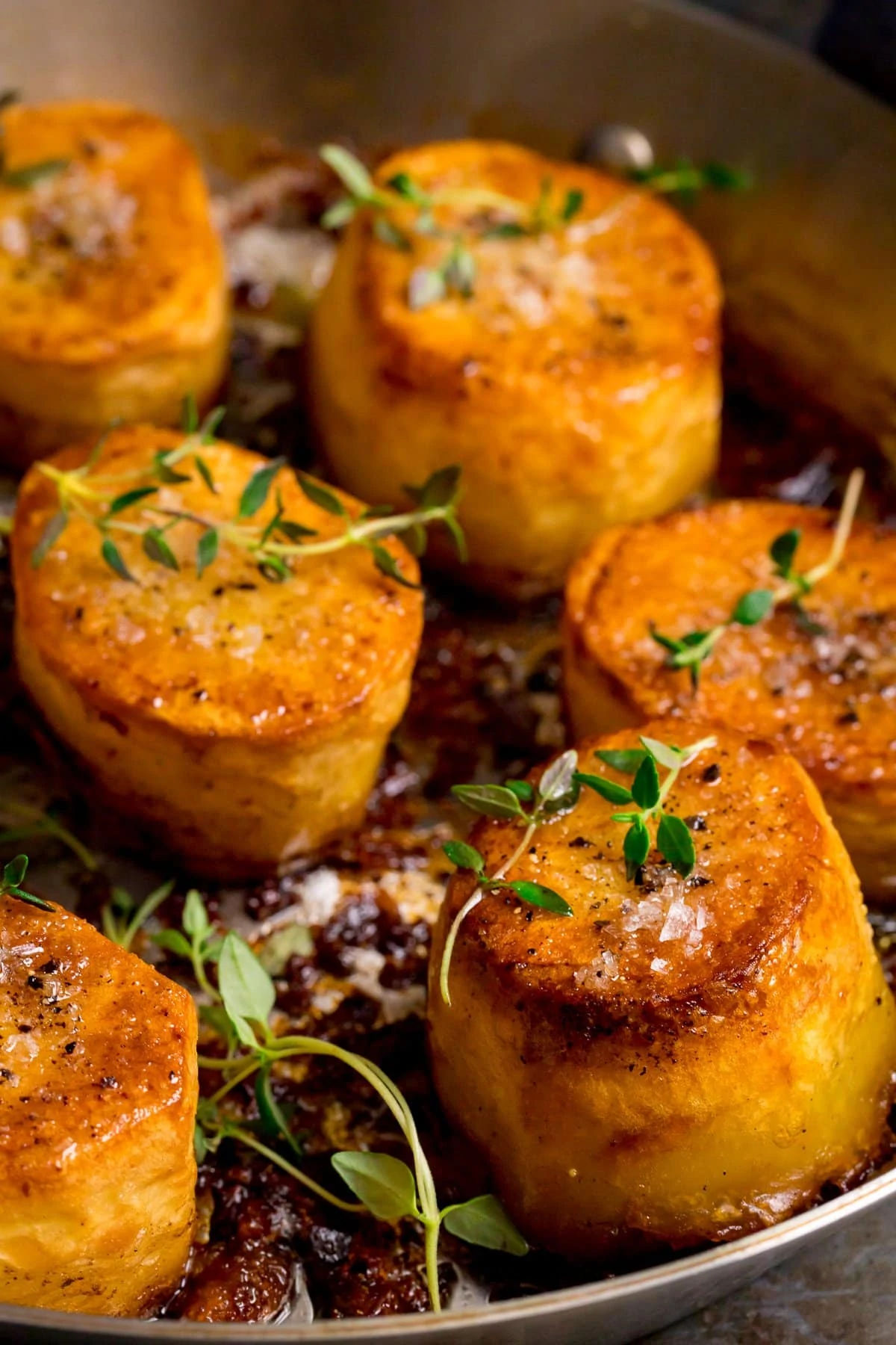 Close up of fondant potatoes in a frying pan, topped with fresh thyme