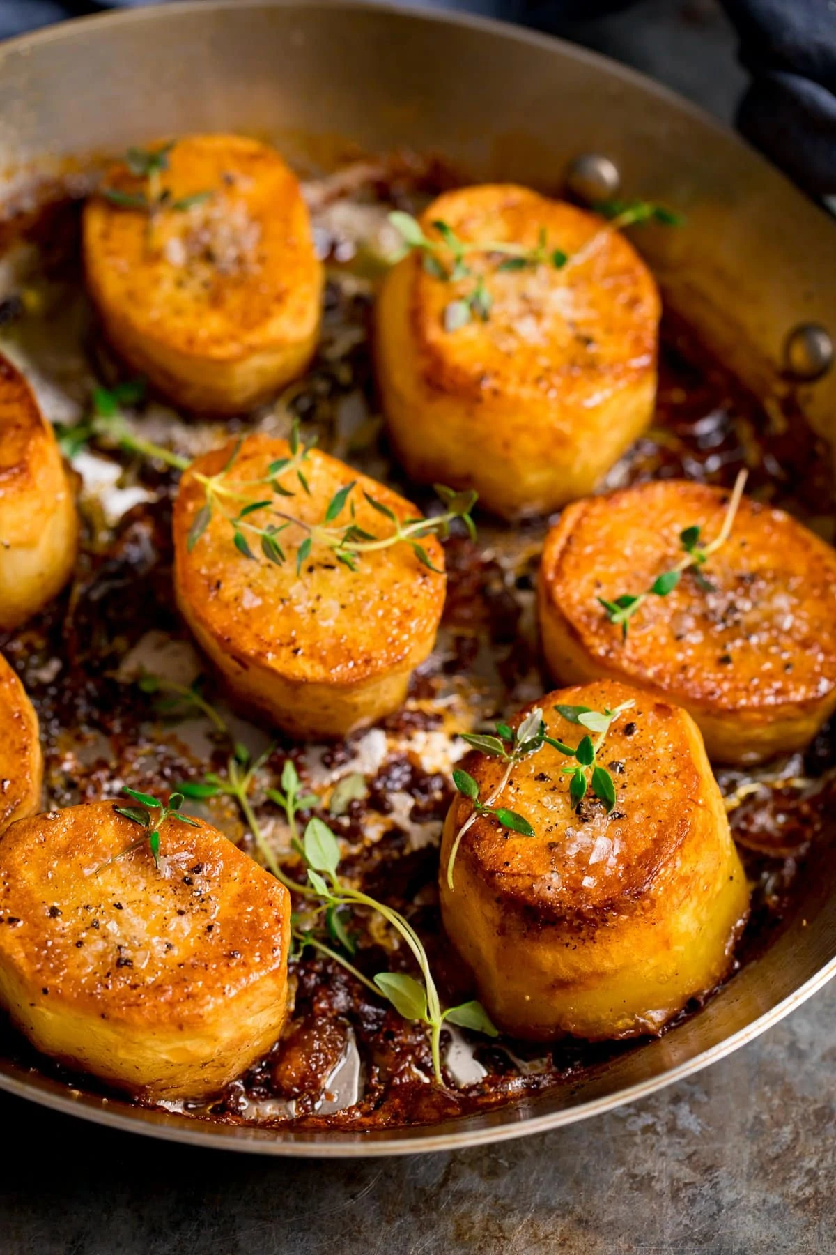 fondant potatoes in a pan topped with thyme and salt