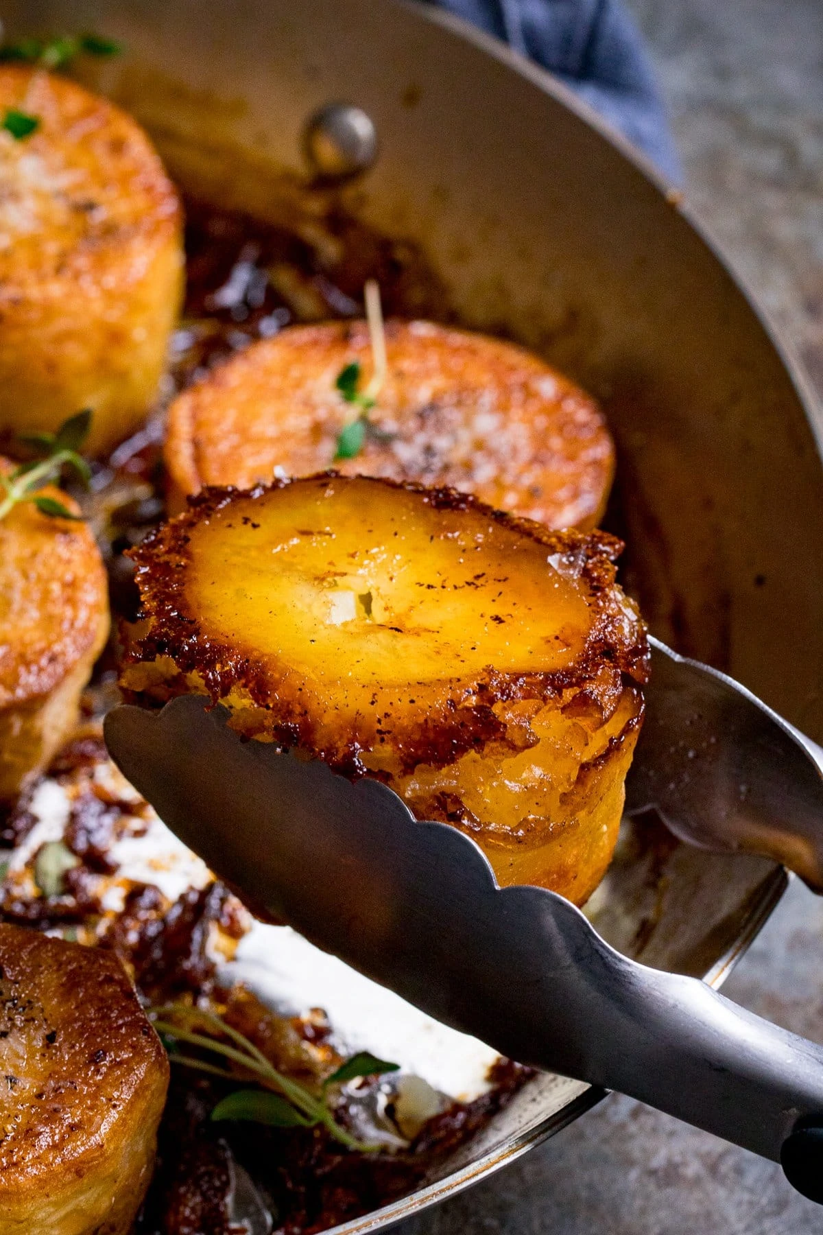 Close up of a fondant potato being taken from a pan with tongs